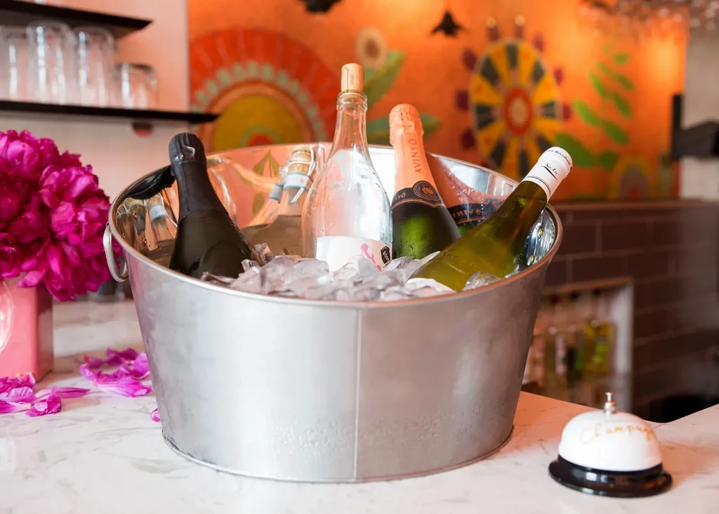 Galvanized ice bucket with sparkling wine, fuchsia flowers, and a champagne bell.