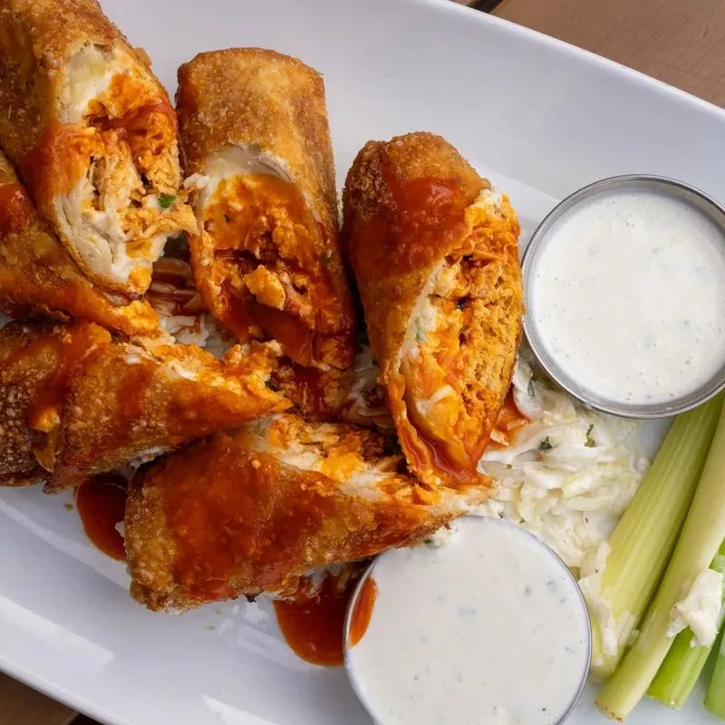 Crispy buffalo chicken egg rolls with two sauces and celery.