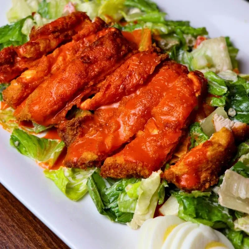 Plate of buffalo chicken strips salad with hard-boiled egg.