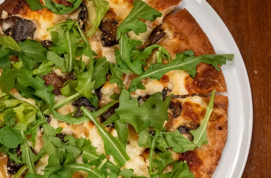 Freshly baked pizza with melted cheese, mushrooms, arugula on wood.