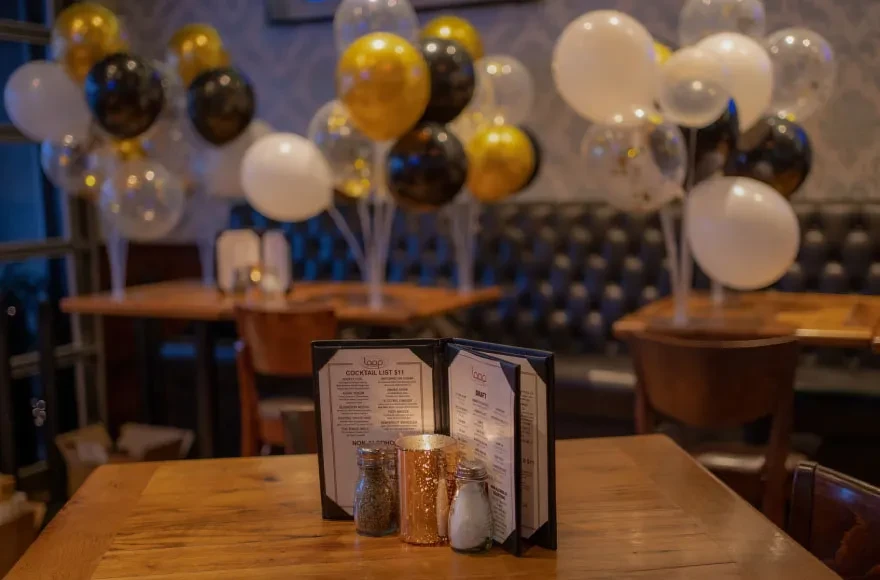 Lit candle, menus, and balloons on tables in a festive restaurant.