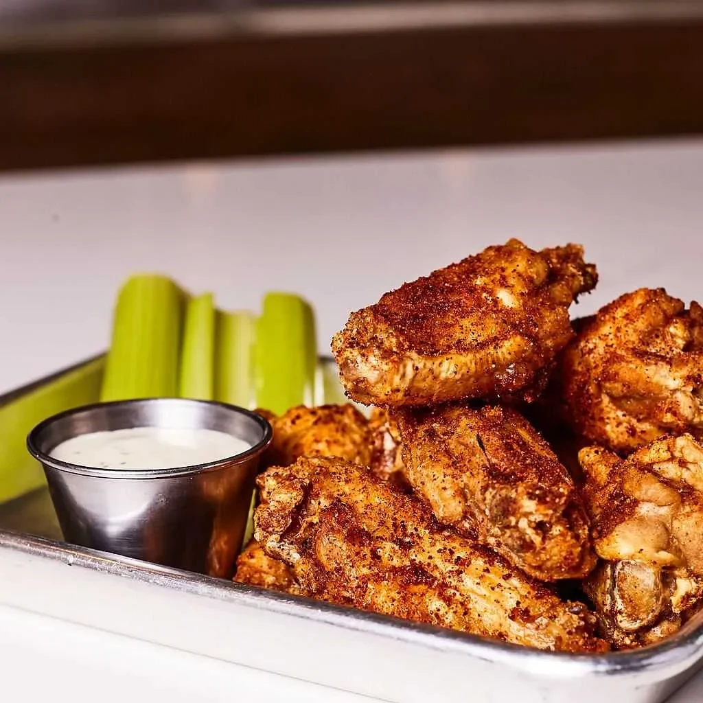 Crispy, seasoned chicken wings on a tray with creamy dip and celery.
