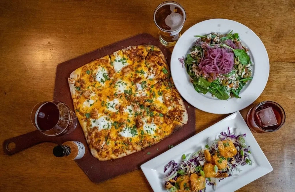 Overhead: Pizza, salad, and drinks on a rustic wooden table.