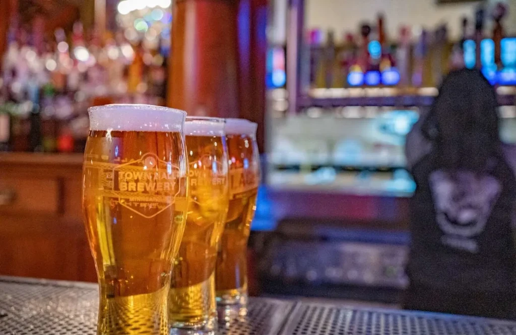 Three pilsner glasses of beer on a dimly lit bar counter.