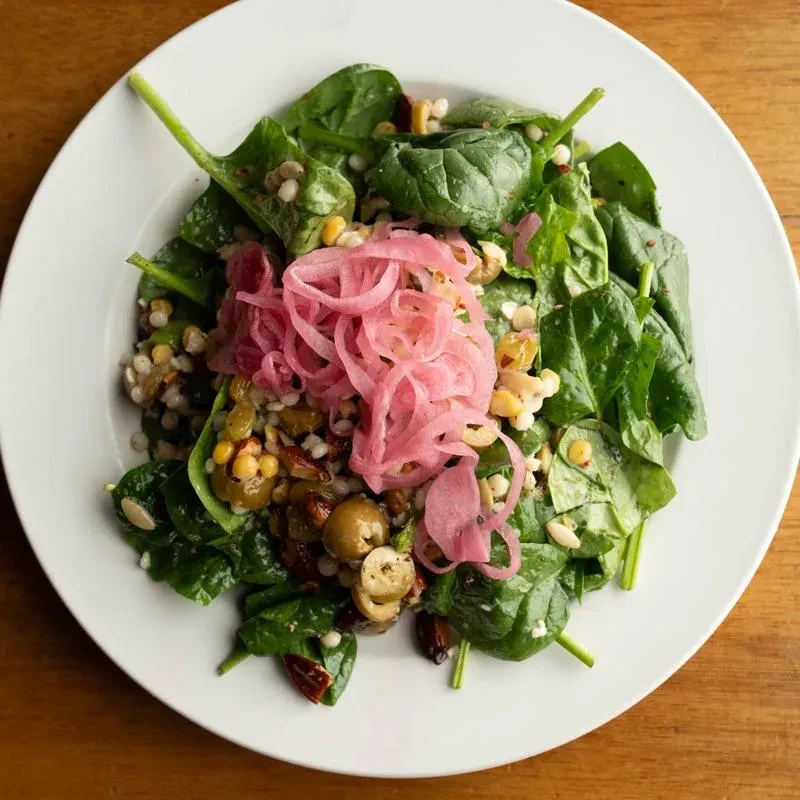 Colorful salad with spinach, prominent pink pickled red onions, and grains.