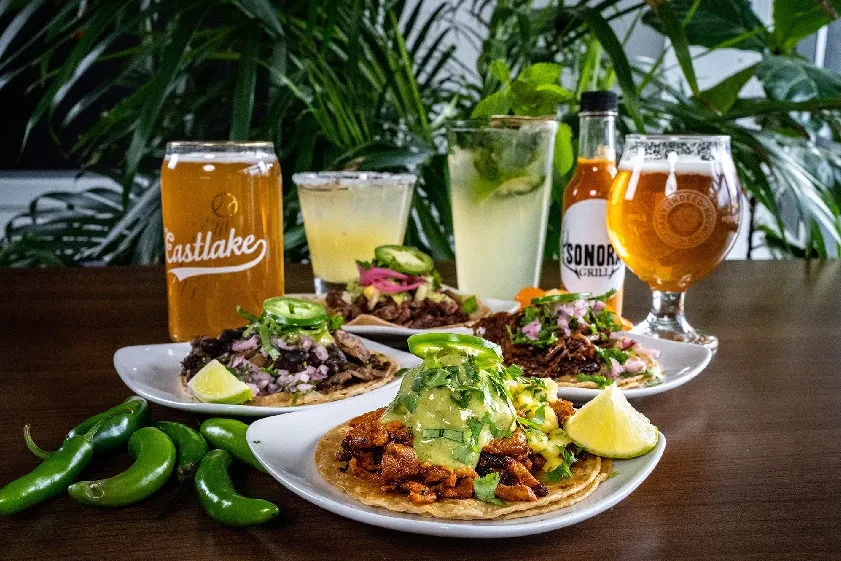 Vibrant Mexican tacos, beers, cocktails, and hot sauce on a table.