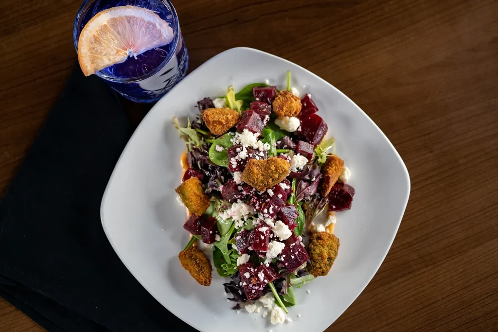 Overhead: colorful salad with beets, feta, greens, golden pieces, and purple drink.