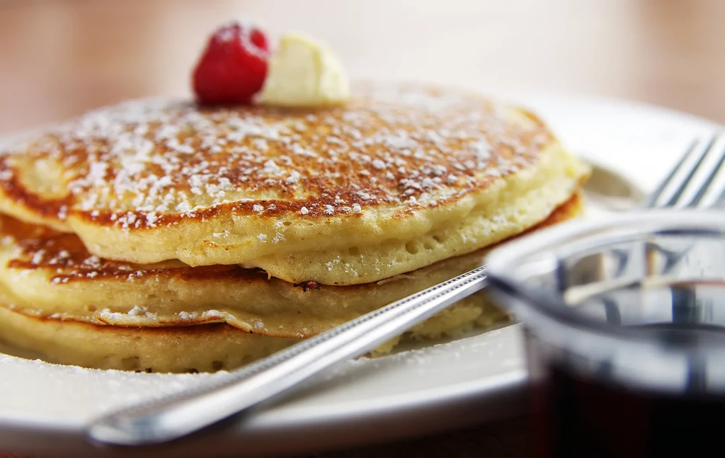 Stacked fluffy golden pancakes with powdered sugar, melting butter, and raspberry.