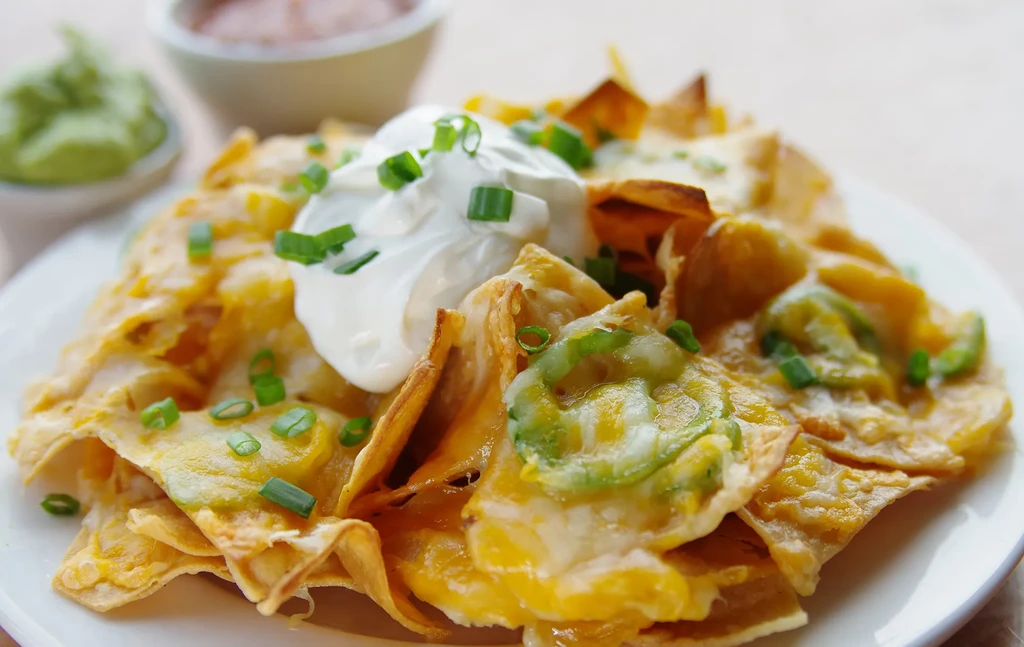 Loaded nachos with melted cheese, sour cream, green onions, and peppers.