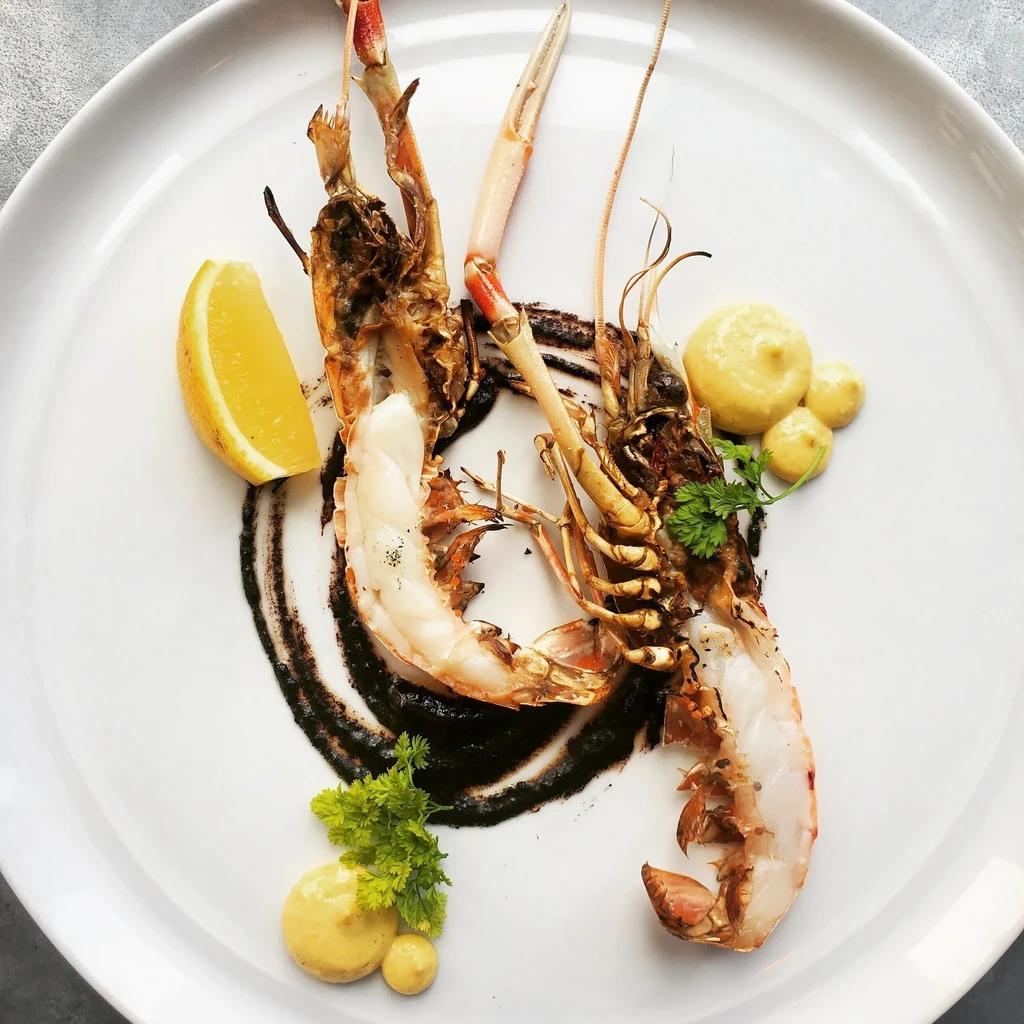 Top-down view of grilled langoustines with dark sauce, lemon, and parsley.