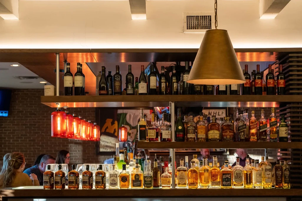 Well-stocked, warmly lit bar area displaying numerous bottles of spirits.