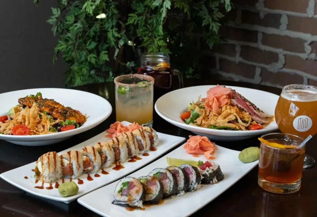 Restaurant table with two salads, two sushi plates, and four drinks.