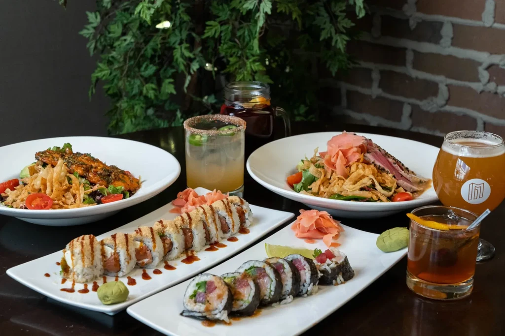 Grilled fish, seared tuna, sushi, and cocktails on a restaurant table.
