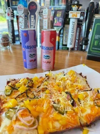 Pizza with pineapple, jalapeño, cheese, and Absolut vodka cans on bar.