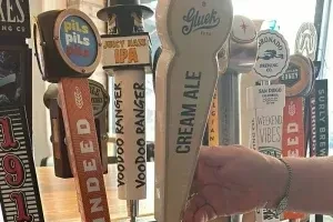 Hand reaching for one of many unique beer taps at a bar.
