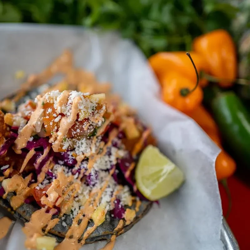 Vibrant taco with purple cabbage, orange sauce, cheese, and a lime wedge.