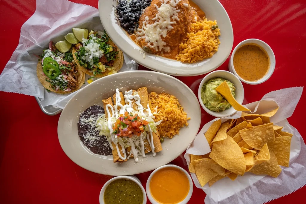 Overhead view of multiple Mexican dishes on a bright red table.