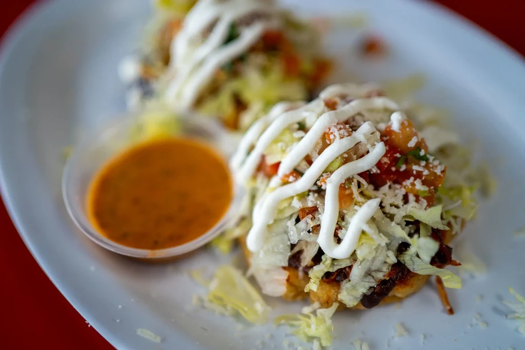 Two sopes topped with lettuce, tomato, cheese, crema, and salsa.