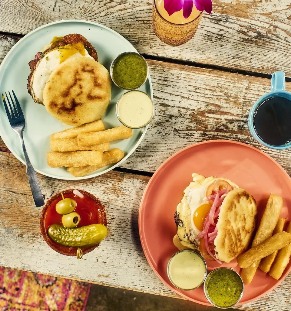 Top-down rustic table with two plates of brunch, sauces, and drinks.