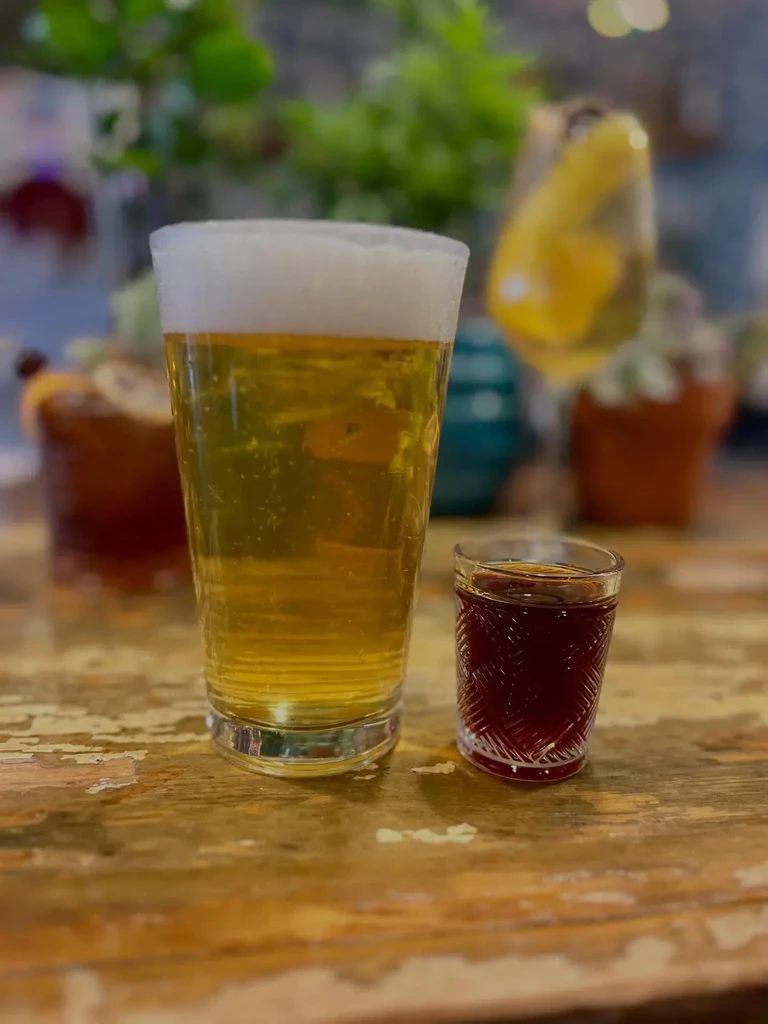 Amber beer, red shot, on a rustic wooden table with blurred background.