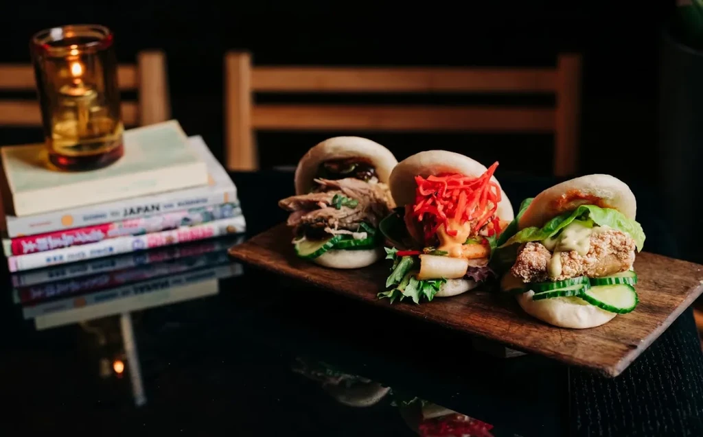 Three gourmet bao buns with diverse toppings on a wooden board.
