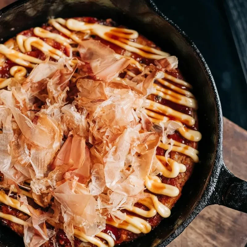 Overhead Okonomiyaki with bonito flakes, dark sauce, and zig-zag mayo.