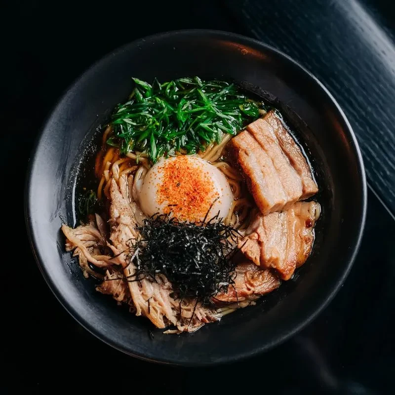 Top-down view of ramen bowl with pork, egg, noodles, vegetables, and nori.
