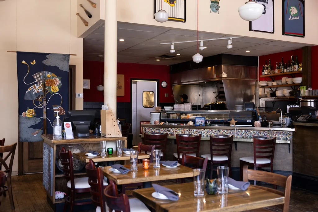 Restaurant interior with set tables, mosaic-tiled sushi bar, and open kitchen.