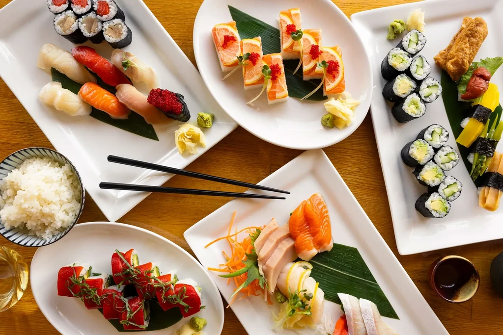 Overhead: Wooden table full of diverse sushi, sashimi, and maki rolls.