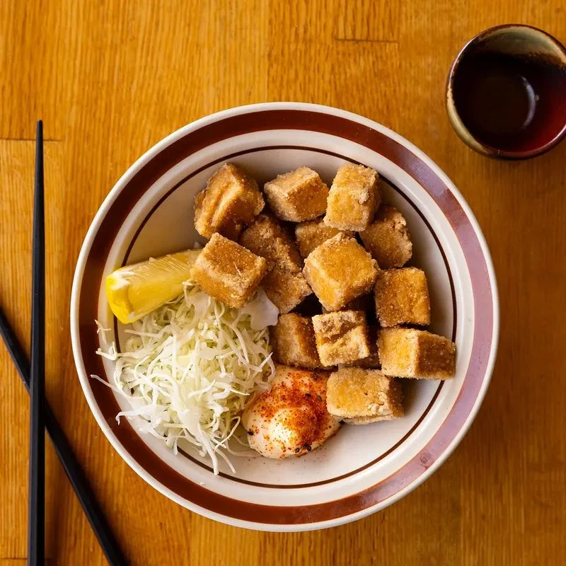 Fried food, cabbage, lemon, egg in striped bowl, with chopsticks.