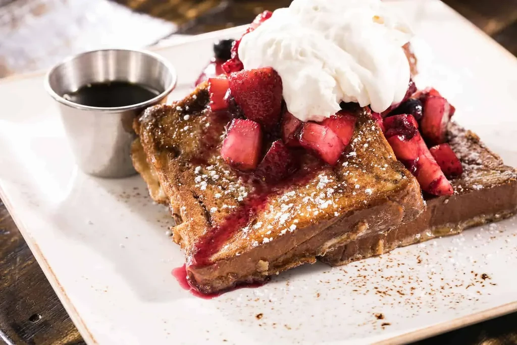 French toast with berries, whipped cream, and syrup on a plate.