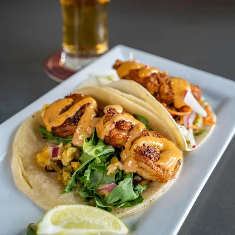Two shrimp tacos with corn salsa, creamy sauce, and lime.