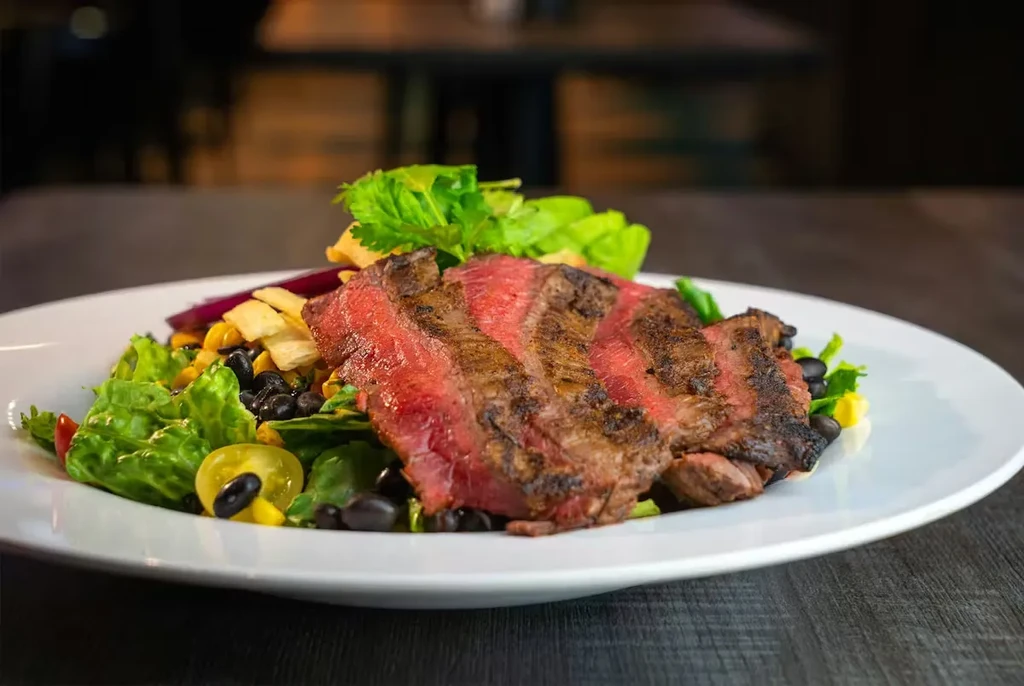 Sliced steak salad with corn, black beans, greens, on a white plate.