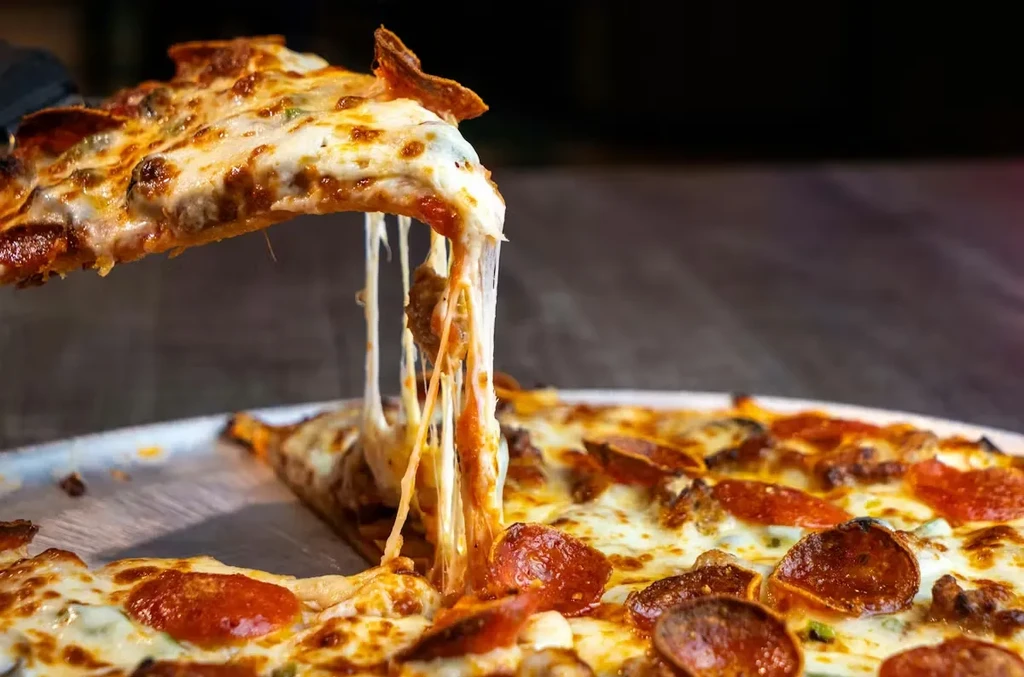 Pizza slice with stretched cheese, pepperoni, and sausage being lifted.