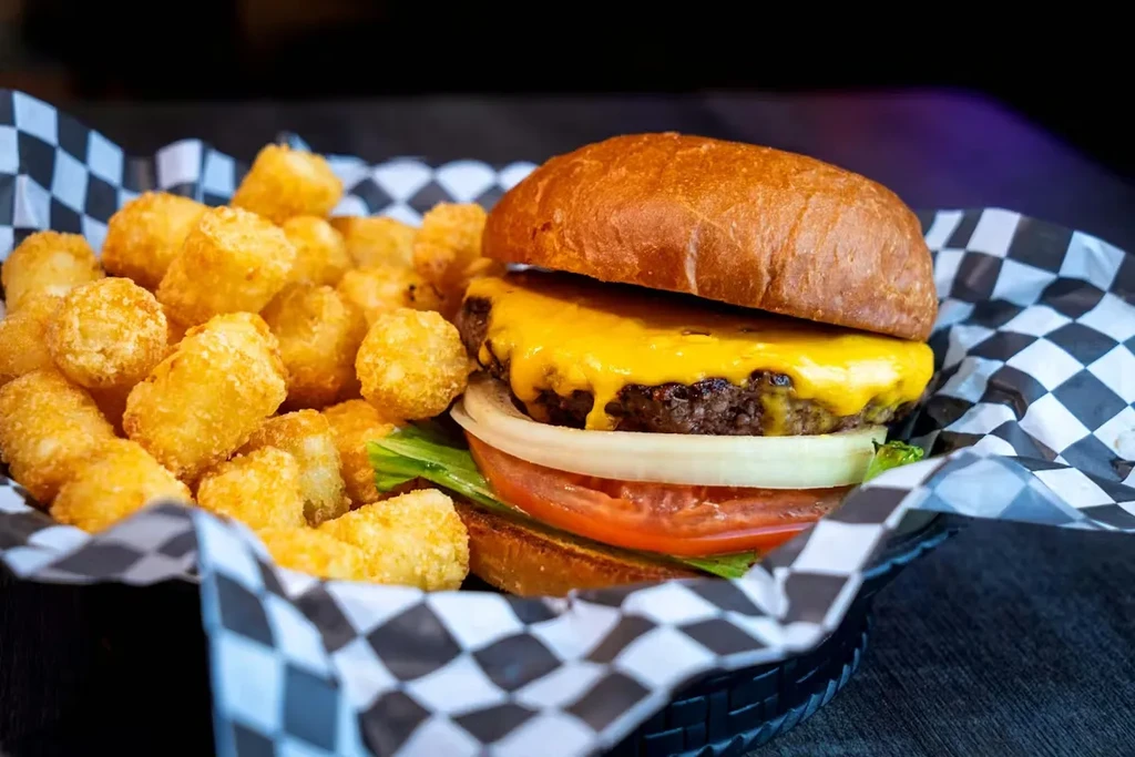 Cheeseburger with melted cheese and crispy tater tots in a basket.