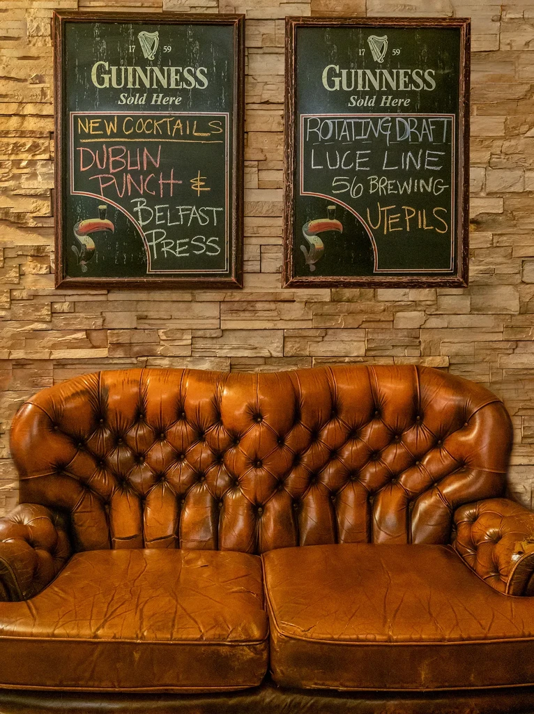 Rustic pub interior with worn leather sofa and Guinness chalkboards.