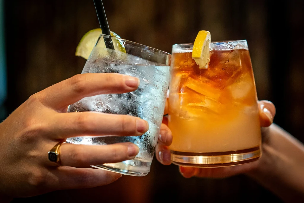 Close-up of two hands toasting drinks with lime and lemon.