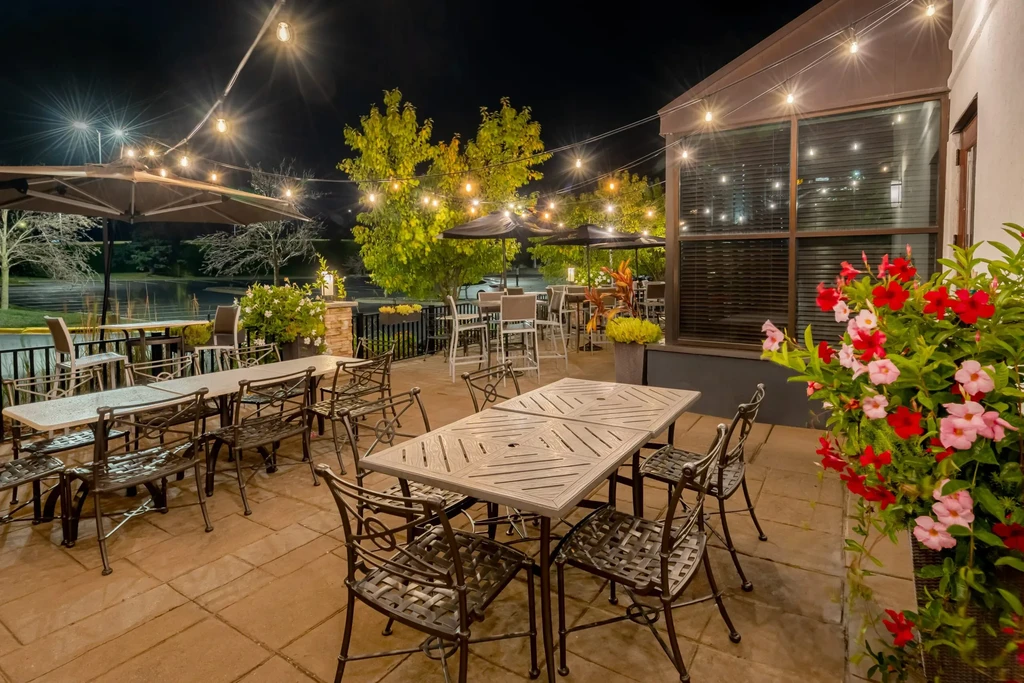 An empty outdoor restaurant patio at night with string lights and water view.