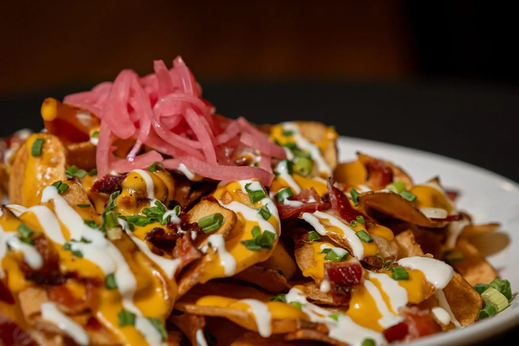 Loaded potato chips with cheese, bacon, chives, red onions, and white drizzle.