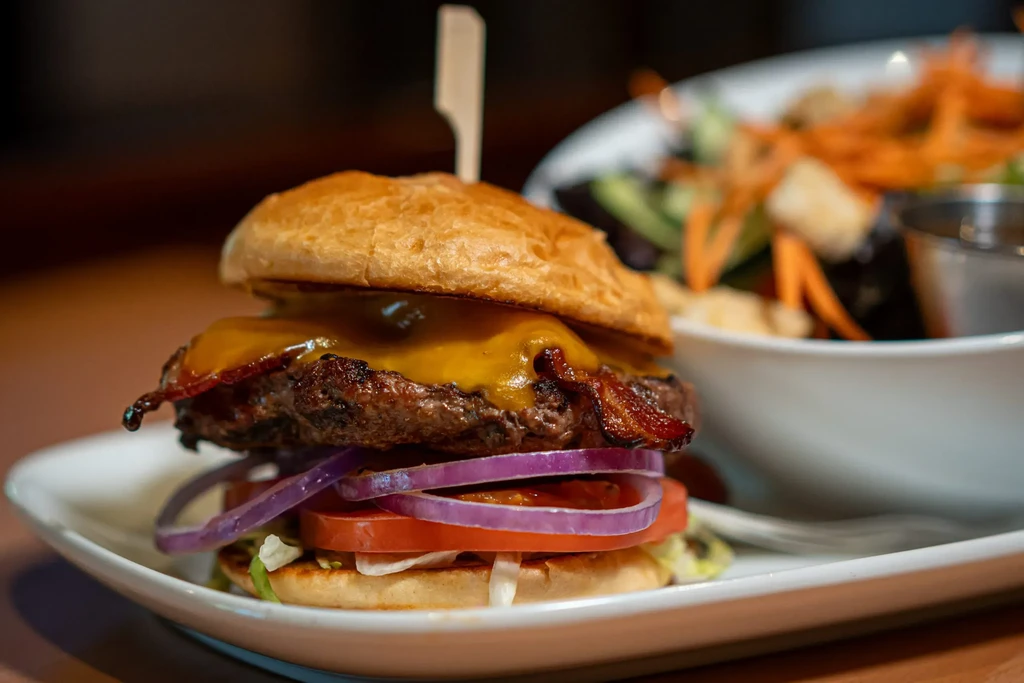 Close-up grilled cheeseburger with melted cheese, bacon, and a side salad.