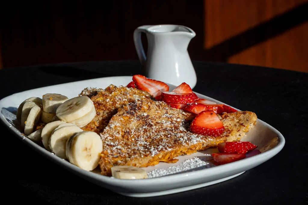 Golden French toast with strawberries, bananas, and powdered sugar.