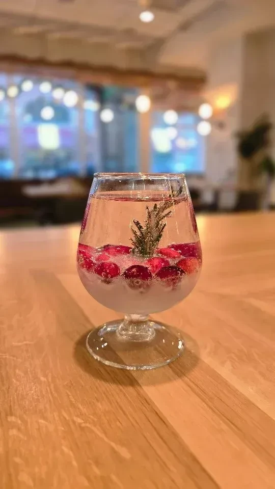 Sparkling pink drink with cranberries, rosemary, and white slush in stemmed glass.