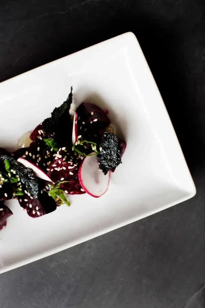 Artfully plated beet salad with radish, herbs, and sesame seeds.