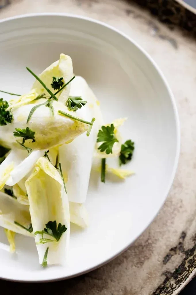 Crisp endive leaves salad with green herbs in a white bowl.