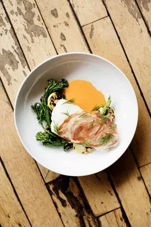 White fish with prosciutto, green vegetables, orange sauce on rustic wood.