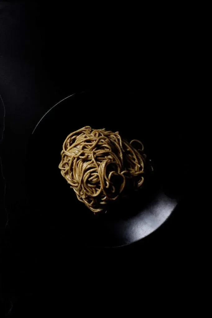 Coiled noodles on dark plate, dramatically lit to glow.