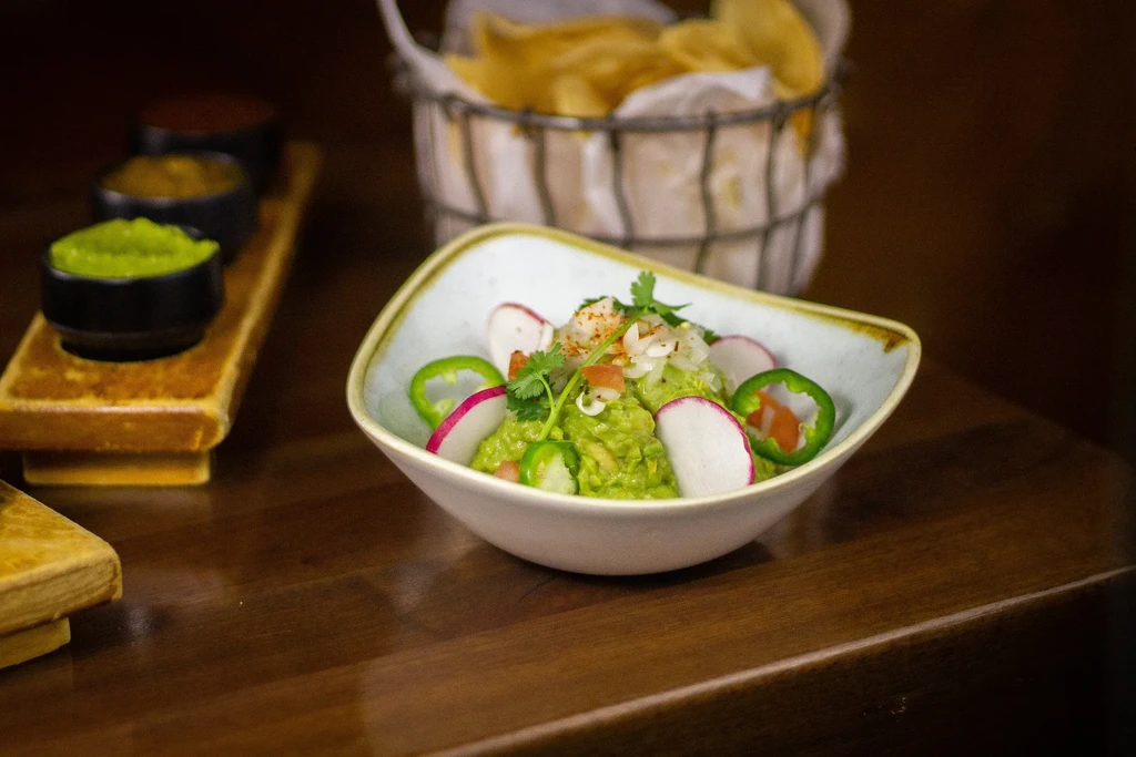 Vibrant guacamole topped with radish, cilantro, jalapeño, and tortilla chips.