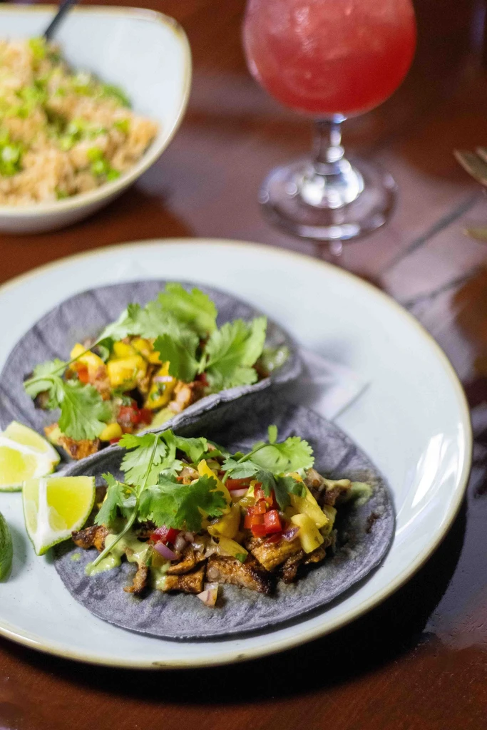 Two dark corn tacos with mango salsa, lime, and cocktail.