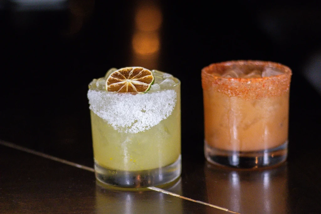 Two cocktails with salt and chili-salt rims on a dark surface.