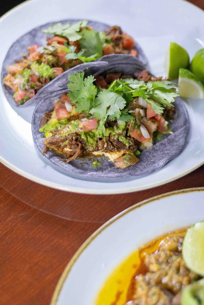 Two vibrant blue corn tacos with meat, guacamole, pico, and lime.